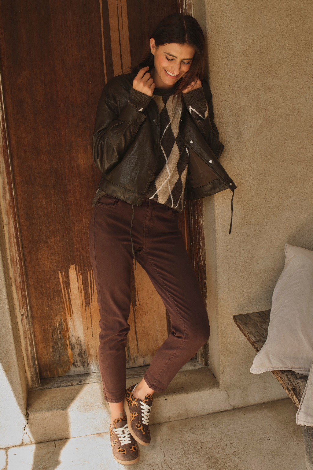 Woman in brown jacket and pants standing against a rustic wall.