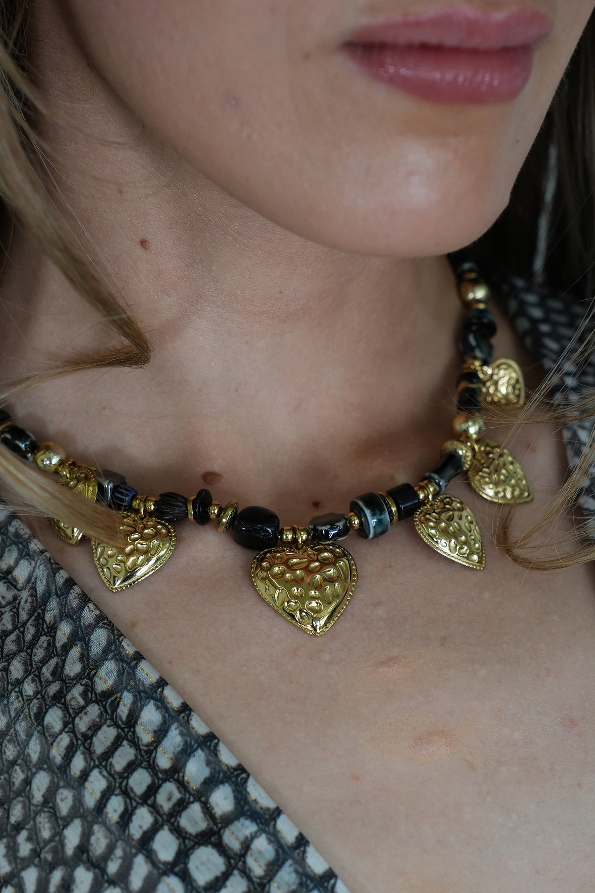 Close-up of a person wearing a gold necklace with heart-shaped pendants.