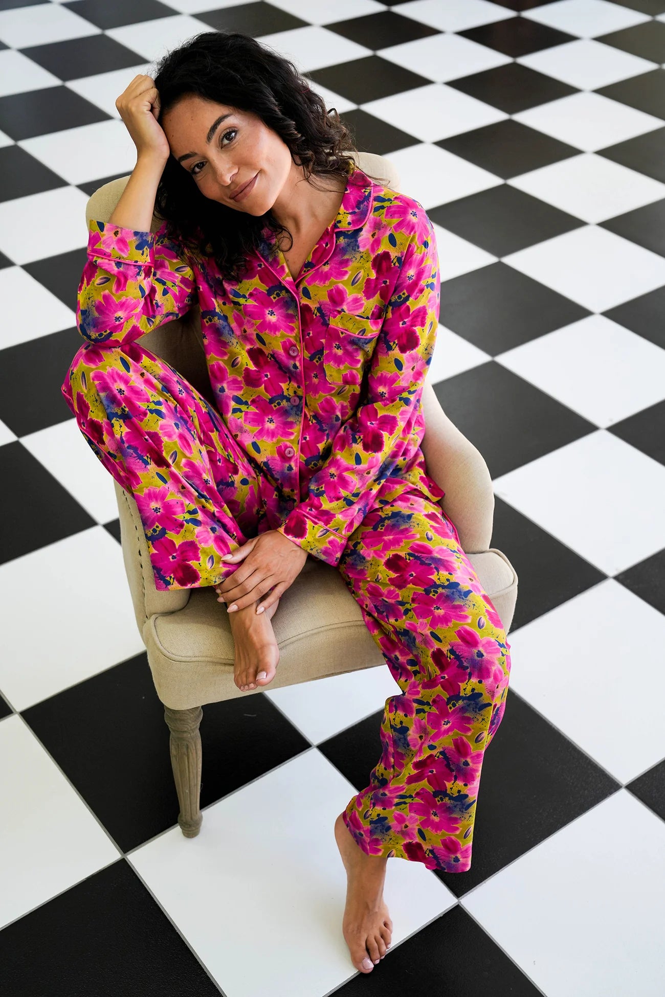 Woman wearing a colorful floral onesie sitting on a chair with a black and white checkered floor.