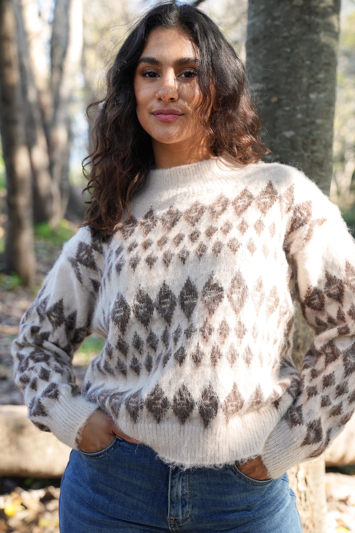 Woman wearing a patterned sweater standing outdoors with trees in the background