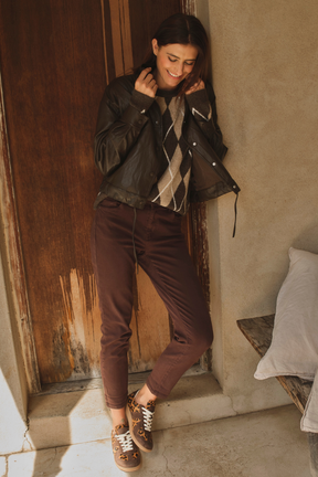 Woman in brown jacket and pants standing against a rustic wall.
