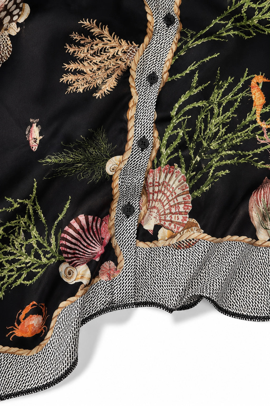 Close-up of a black embroidered fabric with an undersea theme, featuring seashells, coral, seaweed, and small sea life motifs, finished with a gray and white patterned ruffled trim and black buttons.