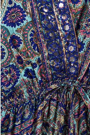 Close-up of a colorful paisley printed fabric with blue, pink, and turquoise tones, featuring a gathered waist tie and decorative mirror-like embellishments.