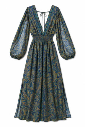 A long-sleeved midi dress with a deep V-neckline, tie-front detail, and a gathered smocked waist, featuring an intricate paisley pattern in blue, teal, and gold tones, shown against a plain white background.