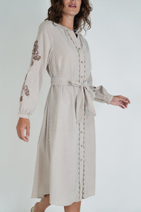 Woman wearing a beige dress with floral embroidery on a white background