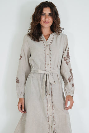 Woman wearing a beige dress with floral embroidery on a white background