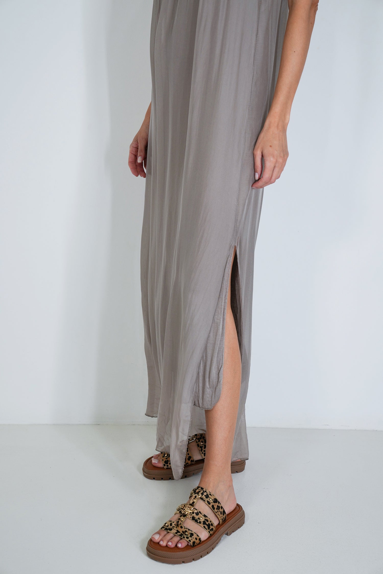 Person wearing a long, light gray dress with a slit on a white background