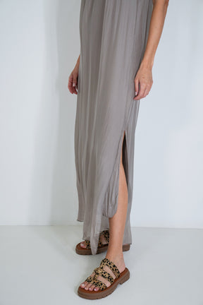 Person wearing a long, light gray dress with a slit on a white background