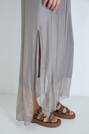 Person wearing leopard print sandals with a flowing gray dress on a white background