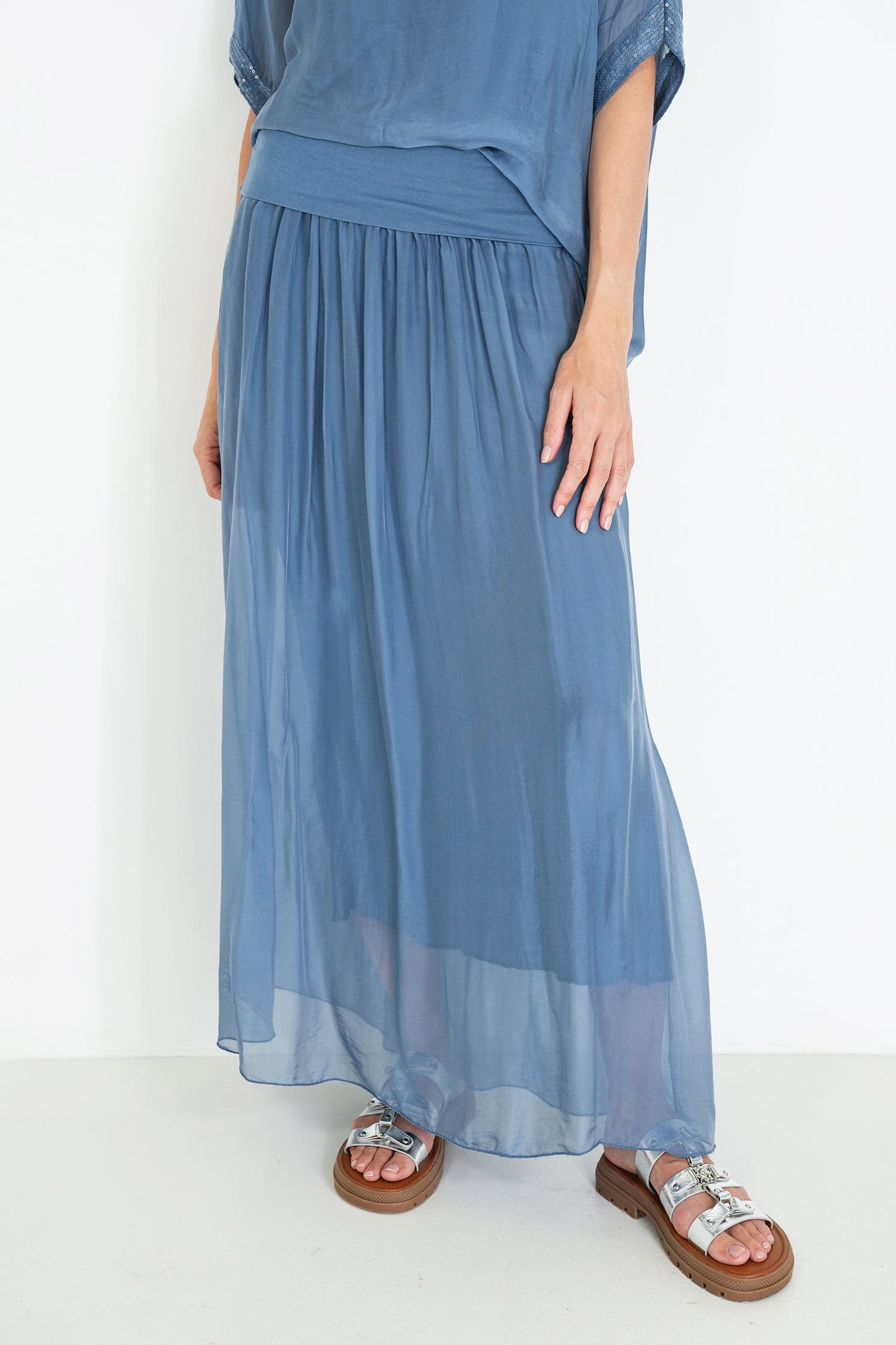 Person wearing a blue silk dress with sandals on a white background