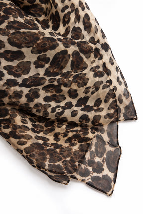 A lightweight leopard print scarf draped on a clean white background, showcasing its beige base with dark brown and black spots.