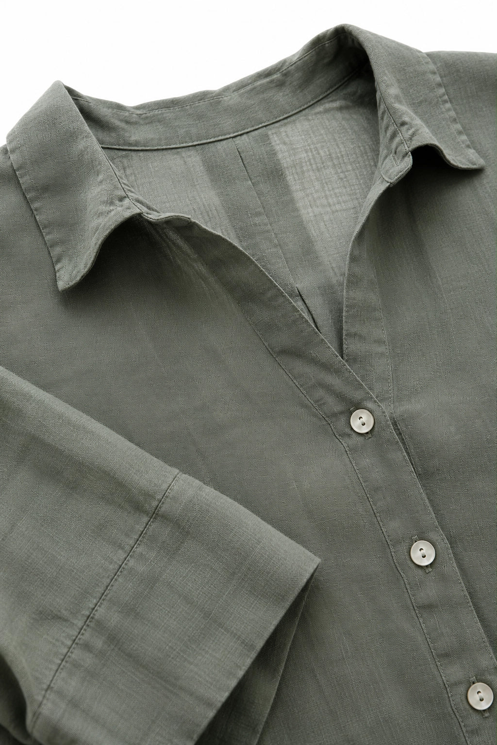 Close-up of a muted sage green linen button-up shirt, showing the textured fabric, collar, and buttons.