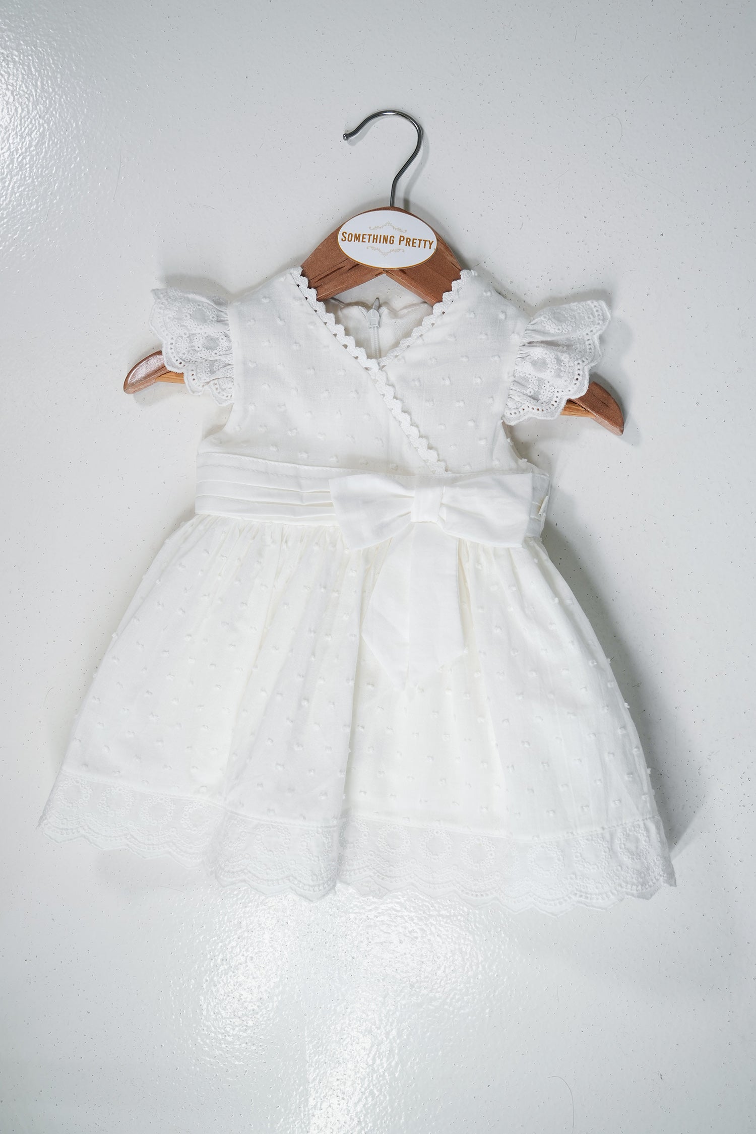 White baby dress with lace details on a wooden hanger against a white background
