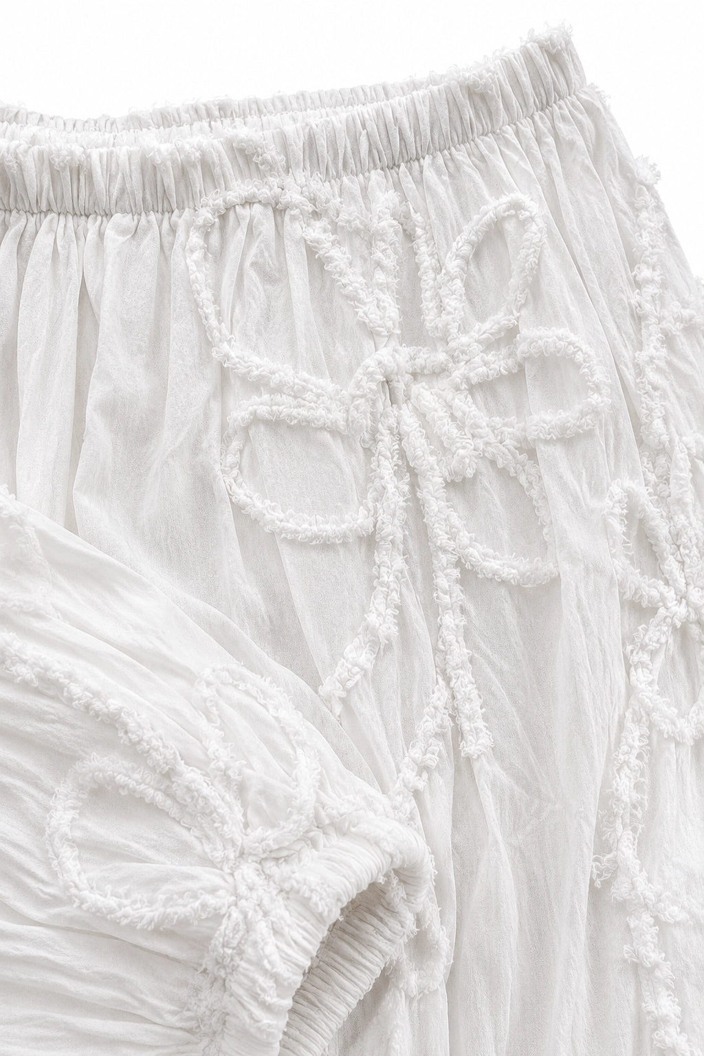 Close-up of white textured fabric with raised embroidered bow details and an elasticized waistband.