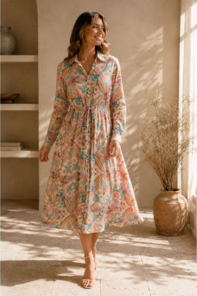 Woman wearing a floral dress in a sunlit room with a vase and plant in the background