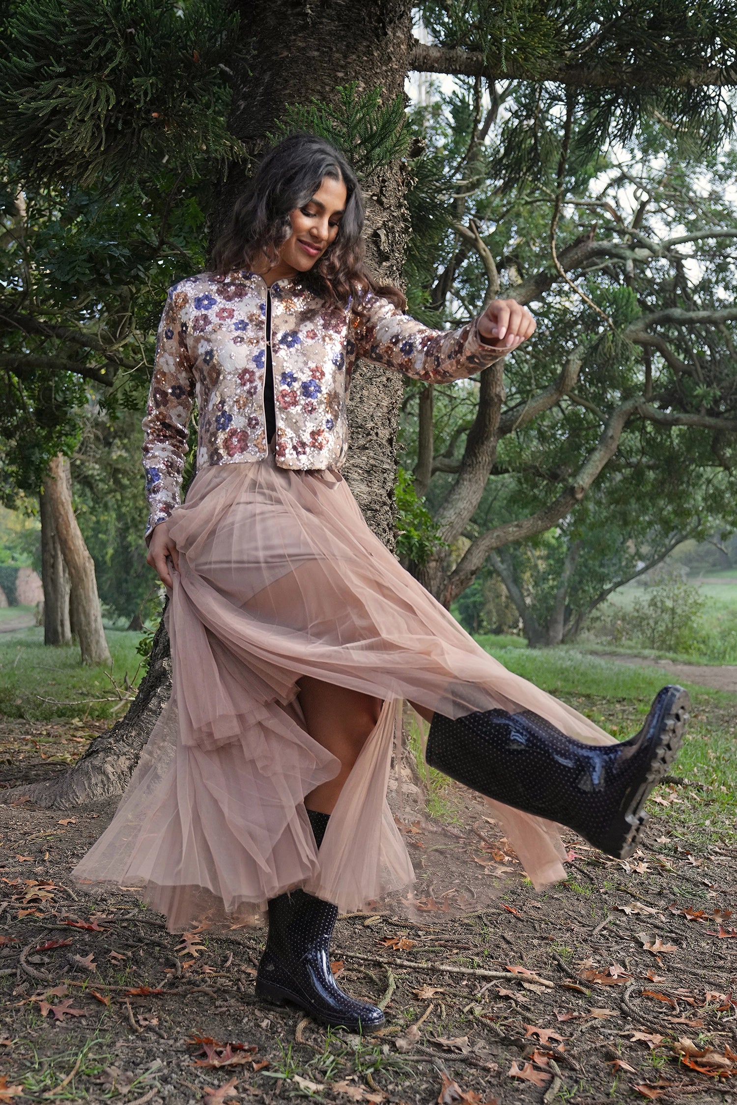Woman in floral blouse and beige skirt with black boots standing in a forest setting