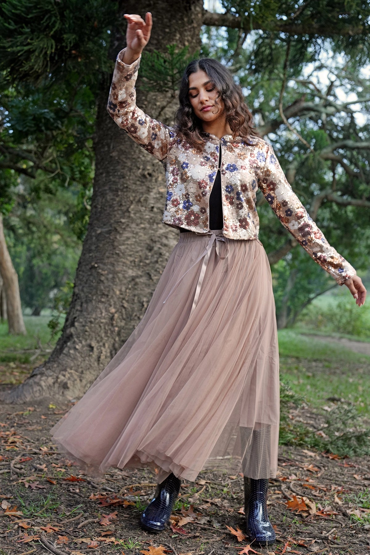 Woman in a floral jacket and beige skirt standing outdoors with trees in the background