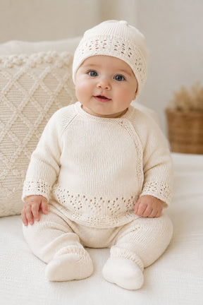 Baby wearing a cream knitted outfit with matching hat on a light background