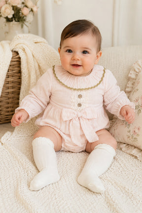 Baby in a pink outfit sitting on a soft surface with a blurred background
