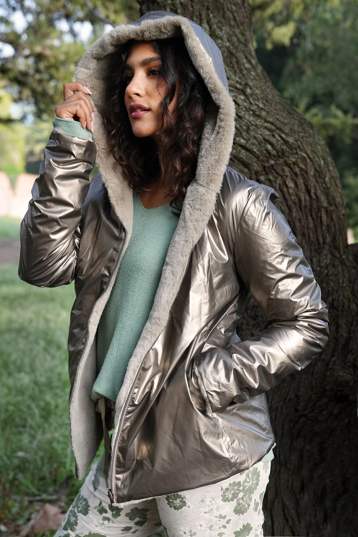 Woman wearing a silver puffer jacket with a hood in an outdoor setting.