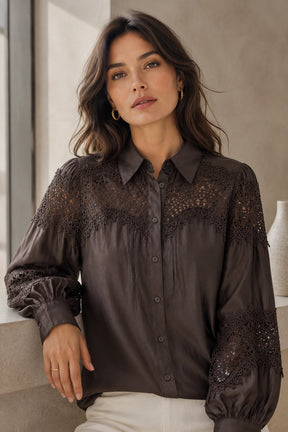 Woman wearing a dark blouse with lace details in an indoor setting