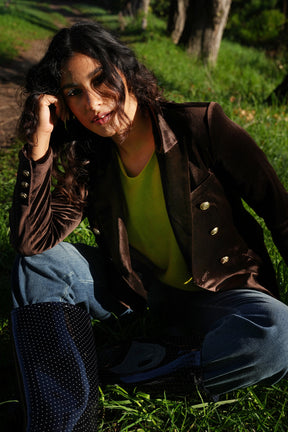Person sitting on grass wearing a brown jacket and blue jeans.