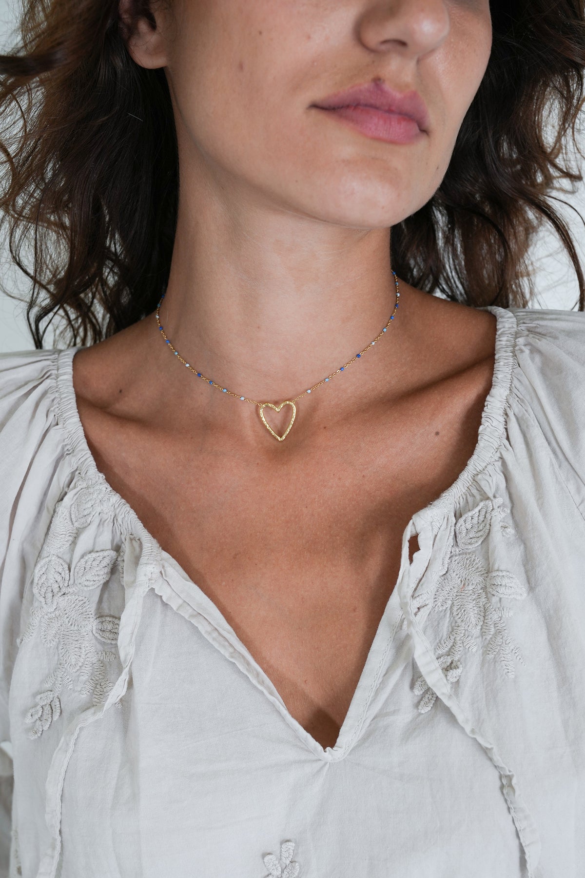 Close-up of a woman wearing a heart-shaped necklace with a light-colored blouse.