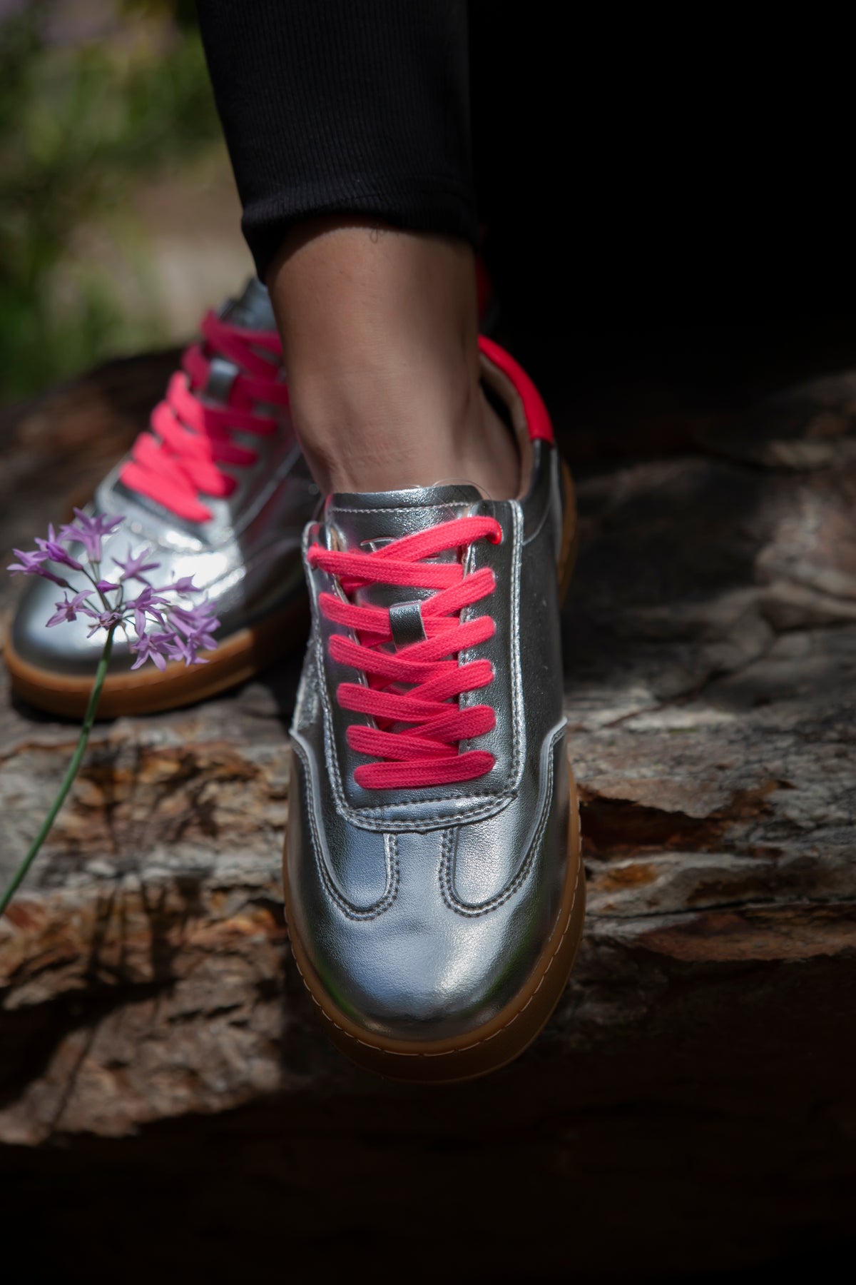 Silver sneakers with pink laces worn on a stone surface