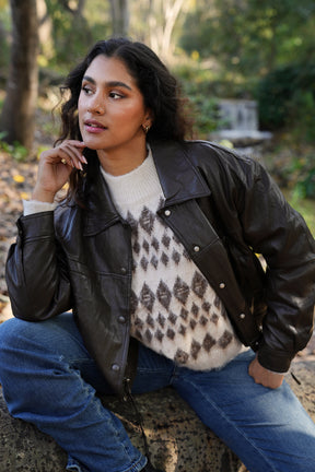 Woman wearing a black leather jacket and patterned sweater sitting outdoors.