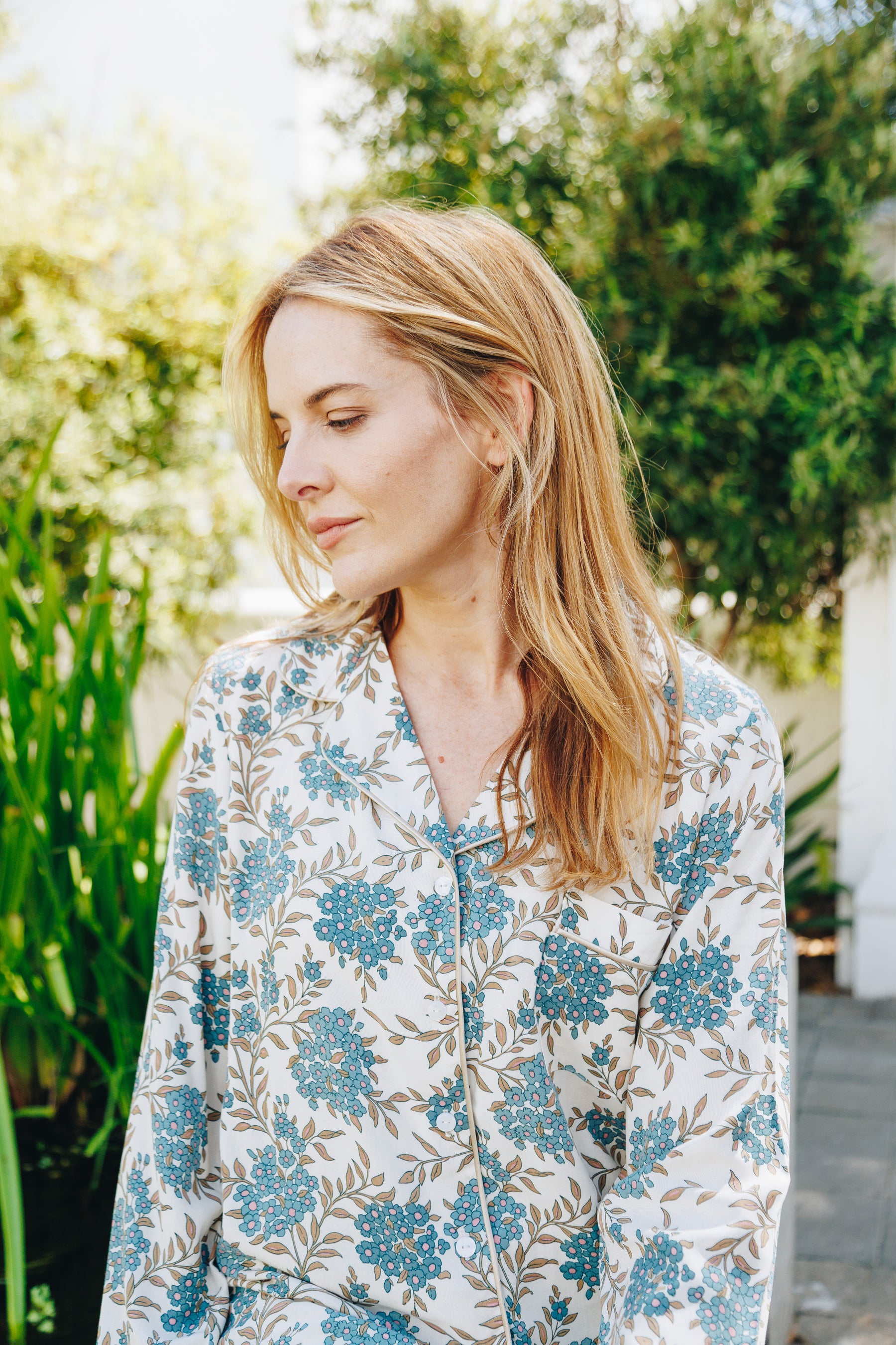 Woman wearing a floral patterned shirt outdoors with greenery in the background